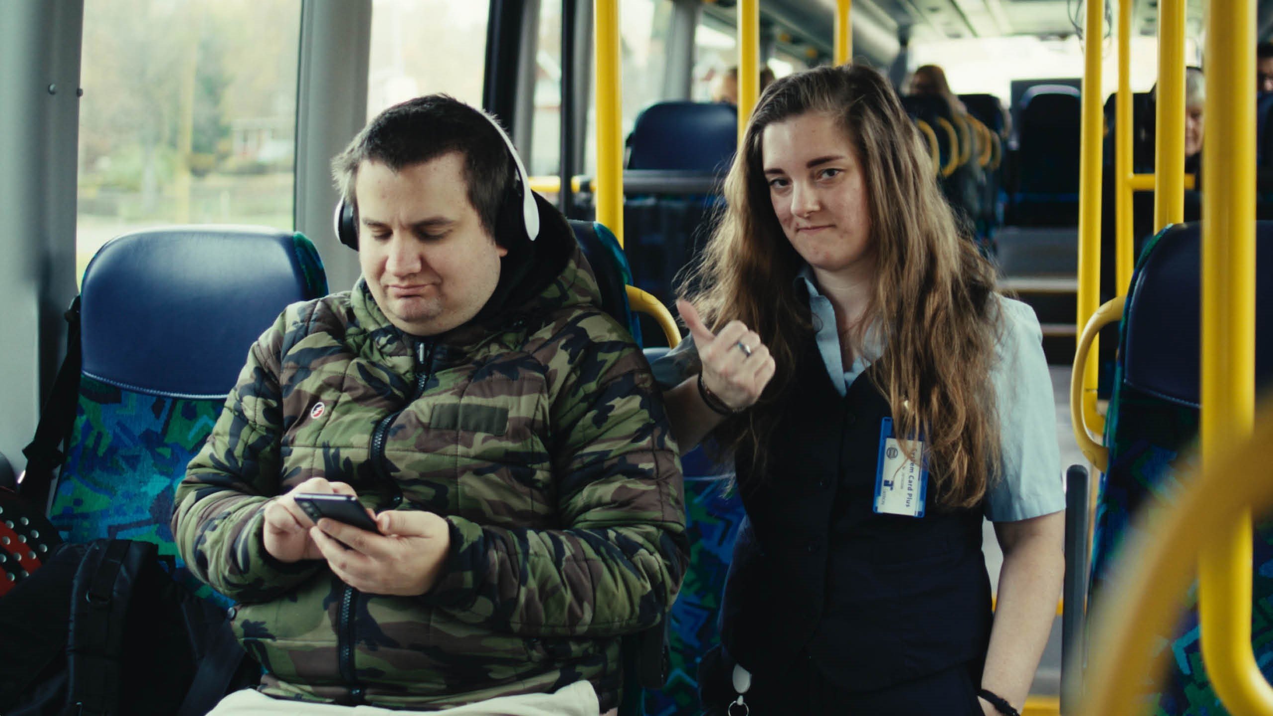 En nöjd bussförare som ger tummen upp till en resenär med hörlurar ombord på en buss